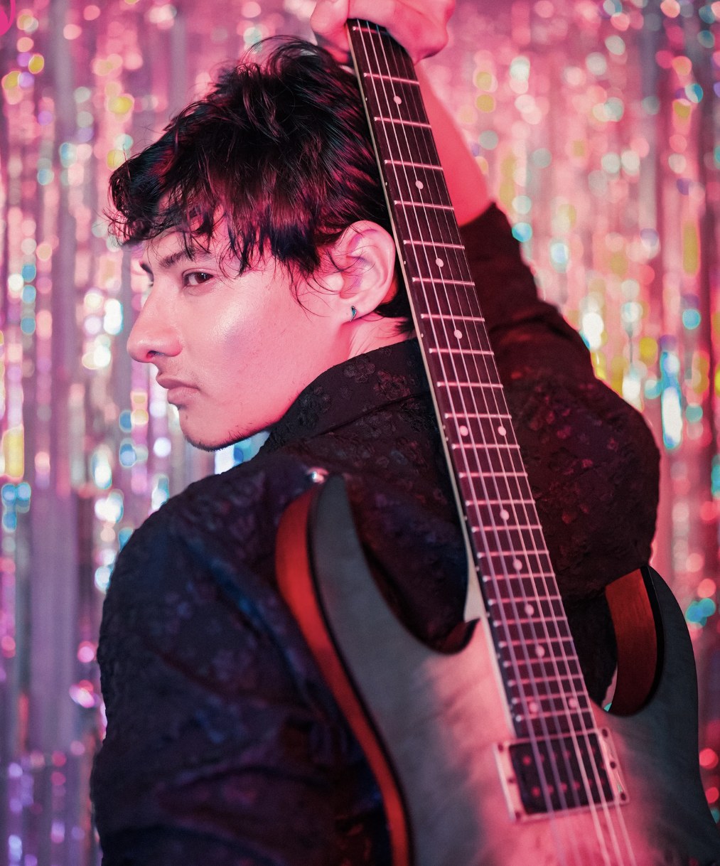 Jay Rana with his guitar against pink lights
